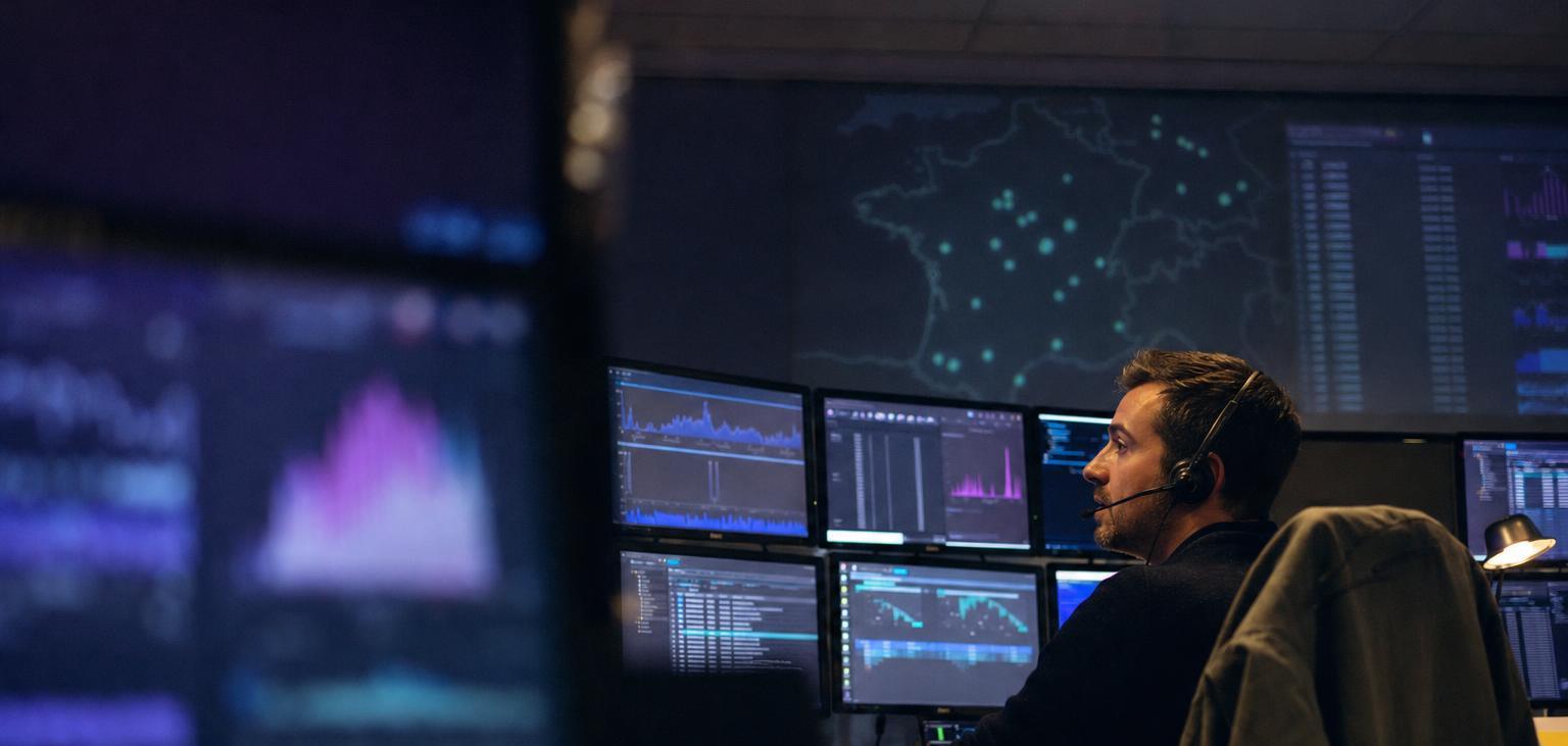 A network engineer with a headset watches traffic graphs at night in a network operations room